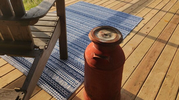 Eine Holzterrasse mit einem Stuhl und einem roten Topf, mit Blick auf einen Fluss.