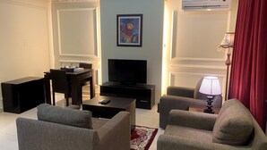 Un salon comprenant un téléviseur à écran plat, une table basse, deux fauteuils, une petite table avec une lampe et un tableau accroché au mur.