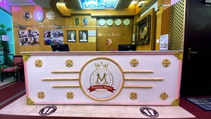 Un comptoir d’accueil orné du logo de l’hôtel Majestic, avec des horloges, des photos encadrées et un panneau indiquant la présence d’un système de vidéosurveillance.