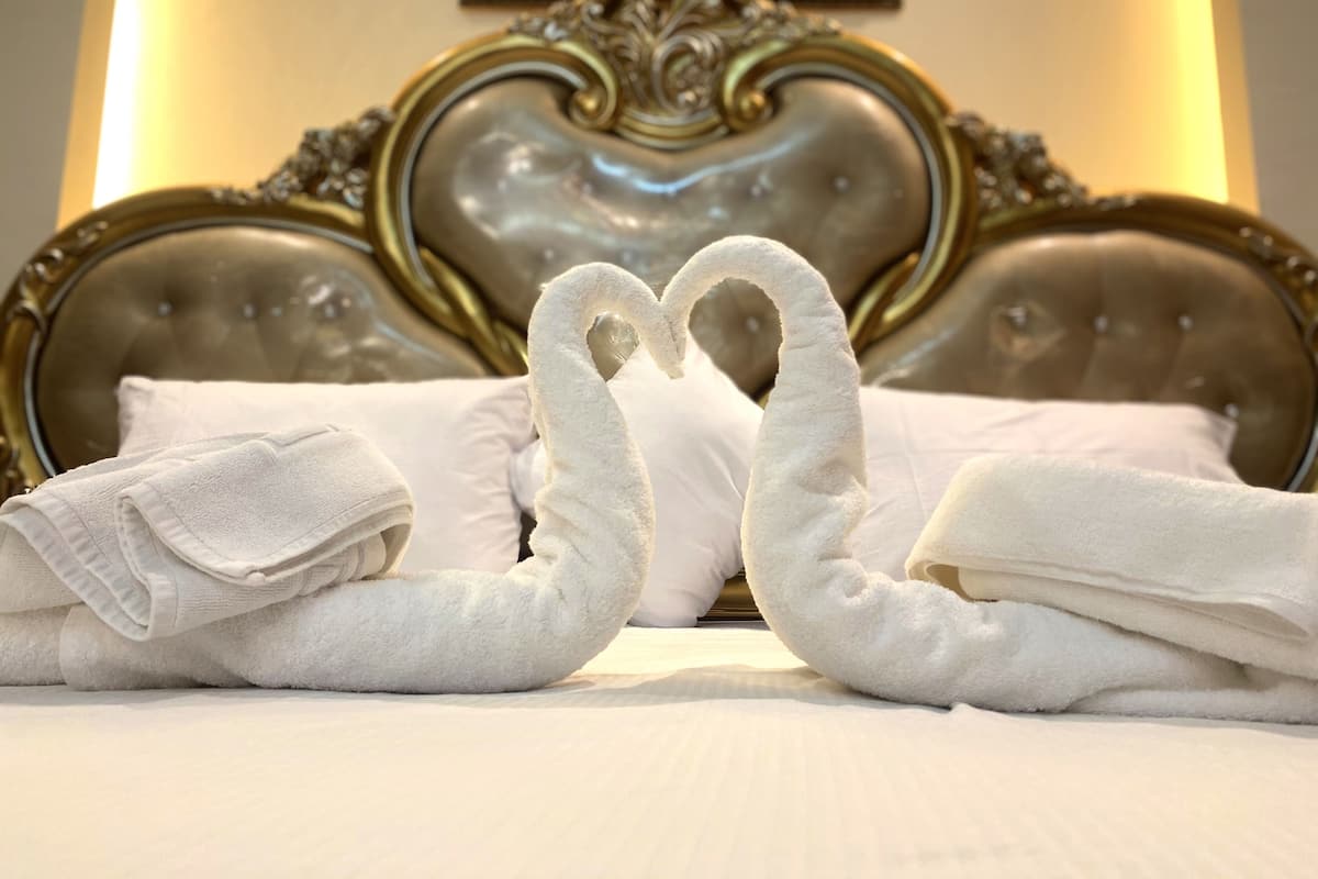 A bed with neatly folded white towels arranged in a heart shape.