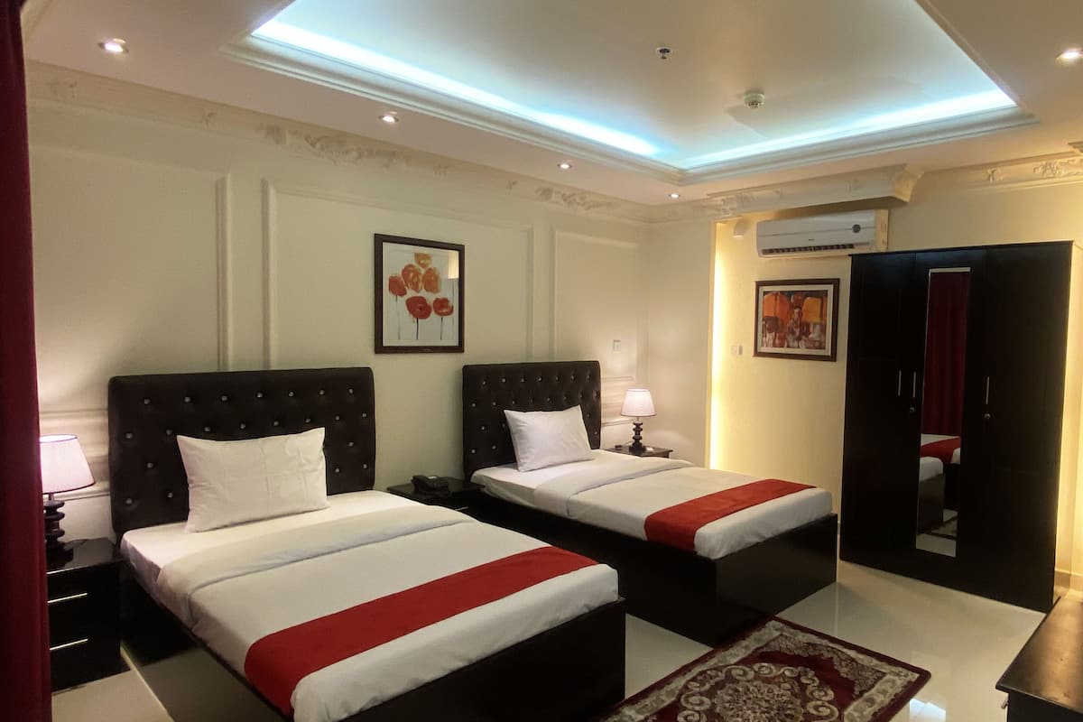 A hotel room with two beds, a red and white bedspread, a nightstand with a lamp, a framed picture on the wall, an air conditioning unit, and a mirror in the corner.