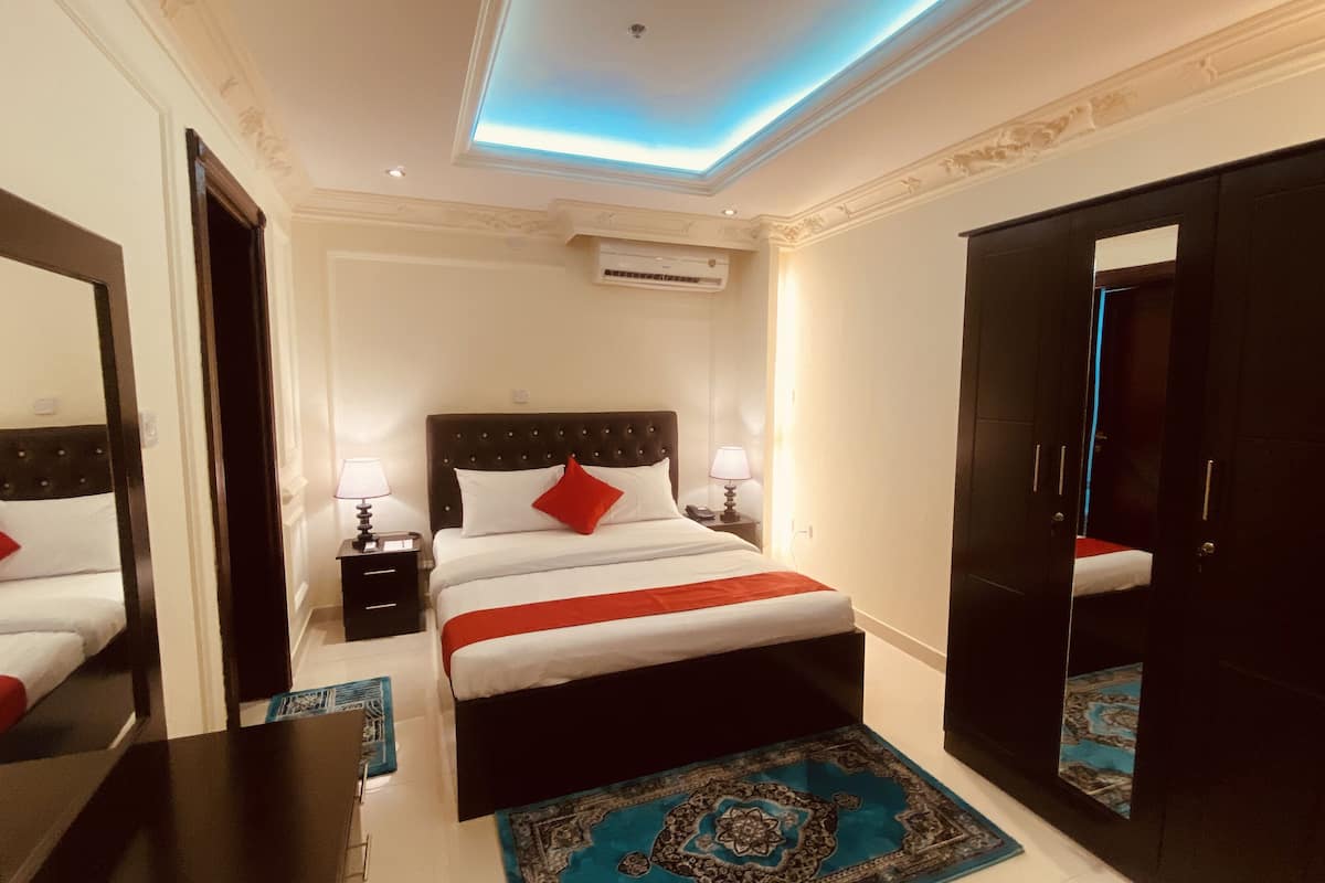 A hotel room with a large bed, two bedside tables, a nightstand, a wardrobe, and a ceiling light fixture.