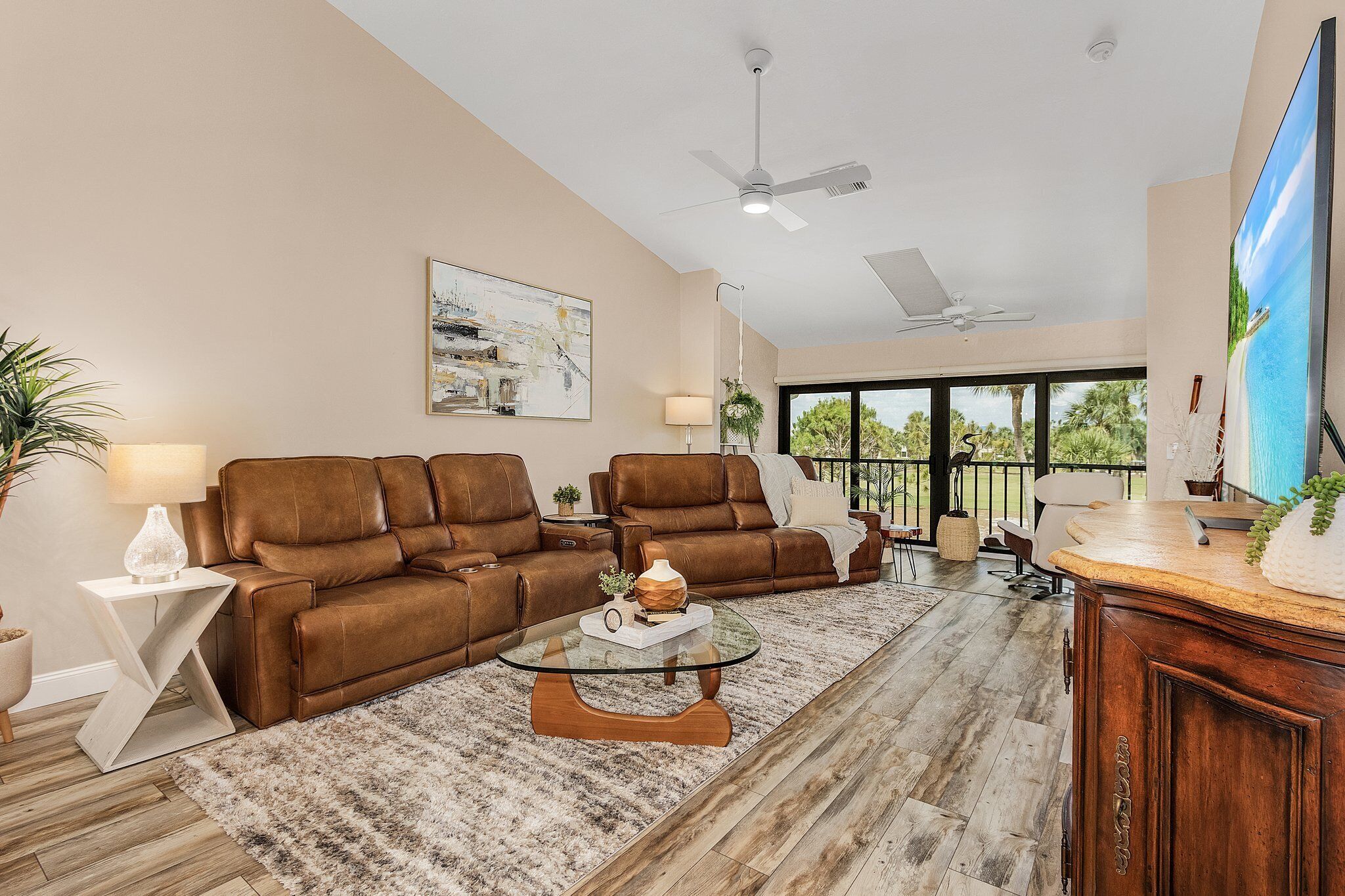 A spacious living room with a brown leather sofa, a glass coffee table, and a wooden cabinet.