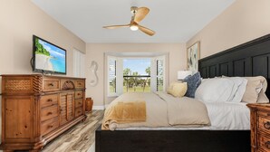 A bedroom with a bed, wooden dresser, TV, ceiling fan, and a view of the outdoors. - Luxury Condo in Gated Golf Community close to Beaches (Fort Myers)