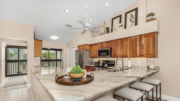 A modern kitchen with a large island, wooden cabinets, and a ceiling fan. - Luxury Condo in Gated Golf Community close to Beaches (Fort Myers)