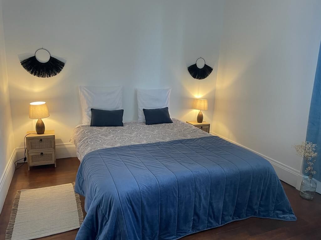 A bedroom with a bed, two bedside tables, and wall-mounted lamps.