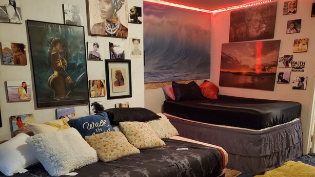 Ein Schlafzimmer mit einem Bett, einer Couch und einer Wand, die mit gerahmten Bildern und einem Wandgemälde dekoriert ist.