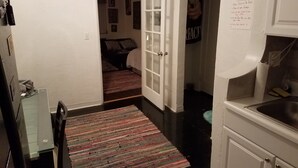 Ein schmaler Flur mit einem gemusterten Teppich, einem Bett im Hintergrund und einer Tür zu einem anderen Raum.