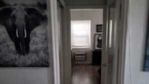 Ein Flur mit Holzboden, weißen Wänden und einer Tür zu einem Zimmer mit Fenster und Klimaanlage.