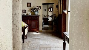 A rustic hallway with stone flooring, wooden beams, and a wooden door leading to a room with a bed and a mirror.