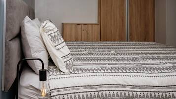 A bed with patterned bedding, a bedside lamp, and a wooden wardrobe in the background.