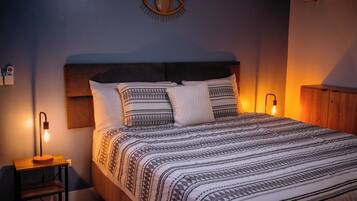 A neatly made bed with patterned bedding, a bedside lamp, and a wall-mounted eye decoration.
