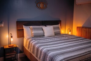 Una cama bien hecha con ropa de cama estampada, una lámpara de noche y un adorno en la pared.