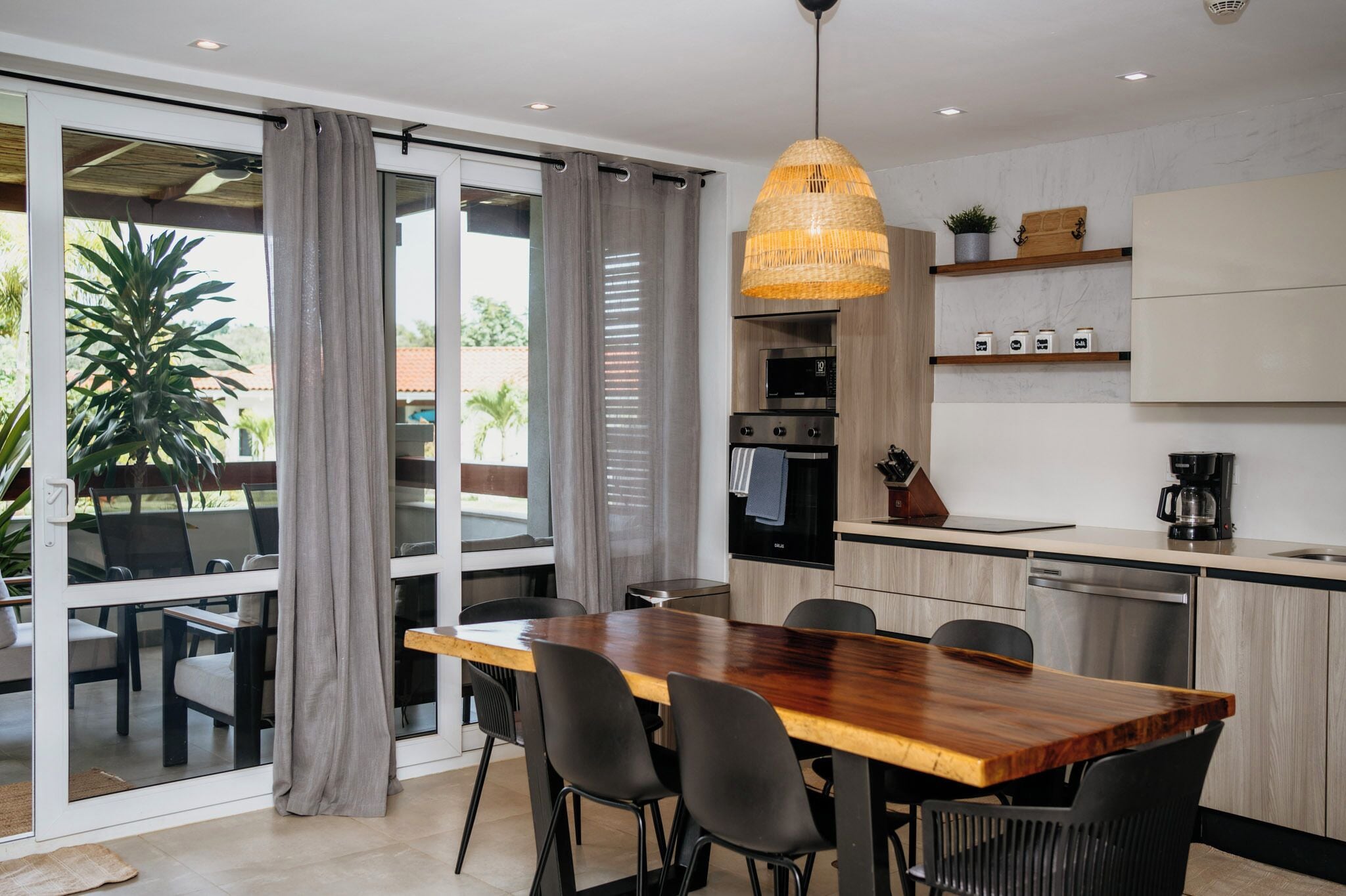 Une cuisine moderne avec une table à manger en bois, des chaises noires et un luminaire suspendu.