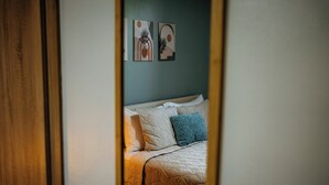 Een bed met een gewatteerde spreidek en kussens, een houten deuropening en twee decoratieve wandobjecten.
