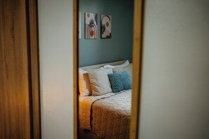 A bed with a quilted cover and pillows, a wooden door frame, and two wall art pieces.