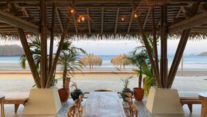 Un área de estar al aire libre con una mesa y sillas de madera, plantas en macetas y vistas a la playa.