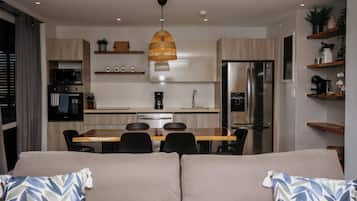 A modern kitchen with a dining area, a sofa with patterned cushions, and a hanging light fixture.