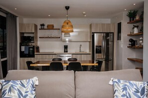 Una cocina moderna con comedor, un sofá con cojines estampados y una lámpara colgante.