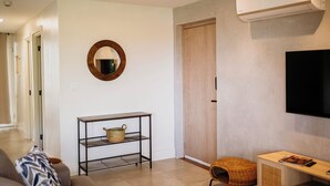 Een moderne woonkamer met een bank, een salontafel, een televisie, een wandairconditioner en een houten deur.