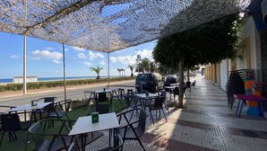 An outdoor seating area with tables and chairs, a view of the beach, and a parked car.