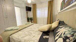 A bedroom with a bed, curtains, a television, and a potted plant.