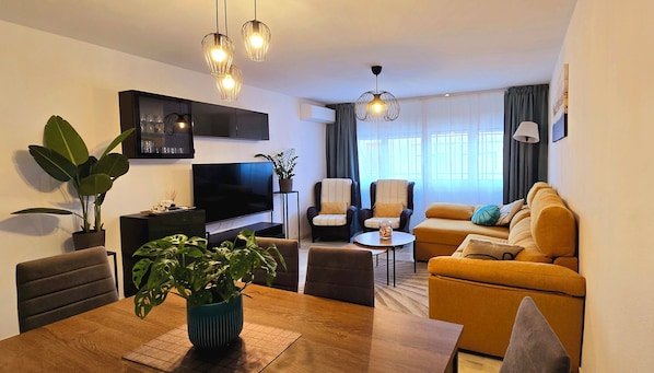 A modern living room with a TV, seating, and plants.