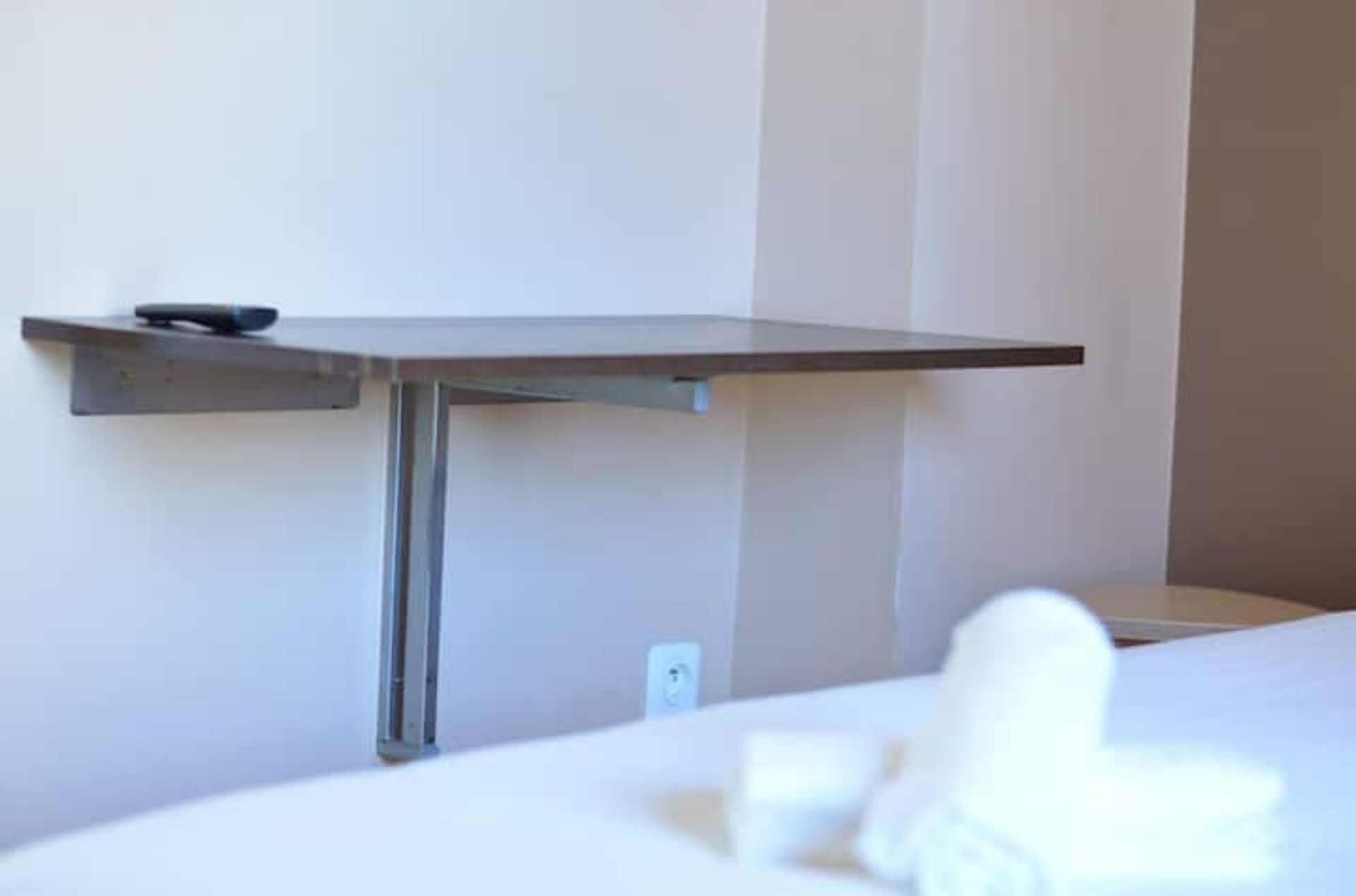 A hotel room with a bed, a bedside table, and a wall-mounted shelf.