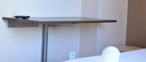 A hotel room with a bed, a bedside table, and a wall-mounted shelf.