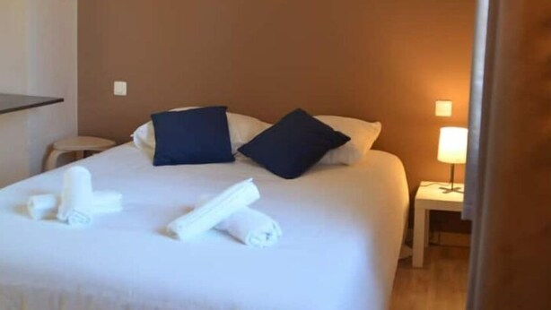 A hotel room with a bed, pillows, a nightstand with a lamp, and towels on the bed.