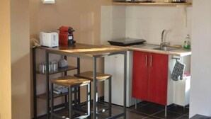 A compact kitchen with a microwave, toaster, and coffee maker on the countertop, a red cabinet, and a small stool.