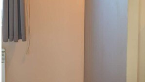 A wall-mounted flat-screen TV in a room with a plain wall and a window with curtains.