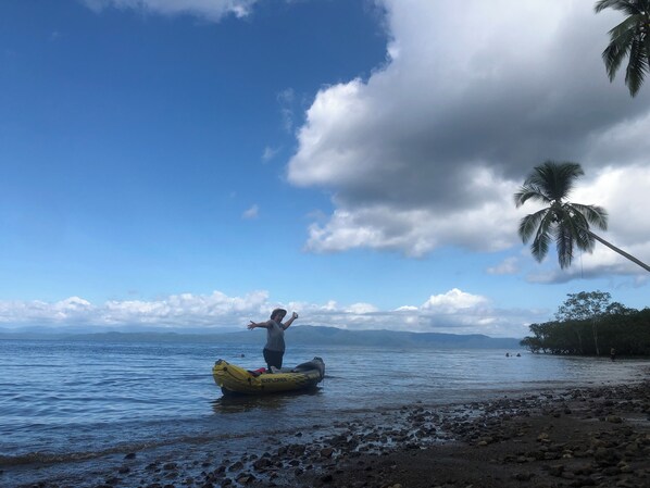 A person standing on a yellow inflatable raft on a rocky beach with a palm tree and a clear sky in the background.