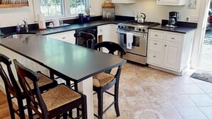 A modern kitchen with a central island, stainless steel appliances, and a dining area with wooden chairs. - Bright, In-Town Nantucket Cottage + Yard - Walk to Main St. (Nantucket)