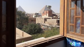 A view through a window of a building with a view of pyramids and a cityscape. - Gohar Guest House (Giza)