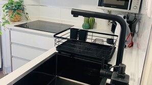 Eine moderne Küche mit weißen Schränken, einer Edelstahl-Spüle, einem schwarzen Wasserhahn, einer Mikrowelle und einem kleinen Topfpflanzen.