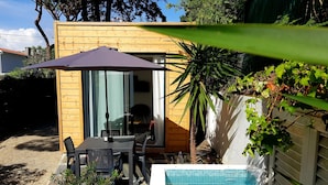 Una cabaña de madera con una mesa y sillas en el patio, una piscina pequeña y plantas en macetas.
