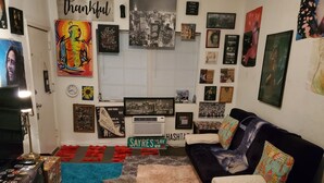 A cozy living room with a black couch, colorful cushions, and a variety of wall art including posters and framed pictures. - Calm Relaxation Haven in SOUTH BEACH MIAMI that is also 420 Friendly. (Miami)