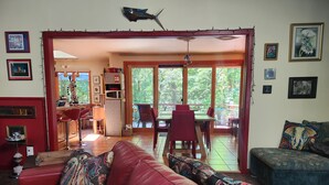 A spacious living room with a red leather sofa, a dining area with red chairs, and a view of the outdoors through large sliding glass doors. - Peaceful, Private Woodland Lot, 5 miles to UNC/Downtown CH. Stay 3 days-3 months (Chapel Hill)