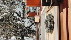 A wooden deck with a railing, a door with a wreath, and a snow-covered landscape in the background.