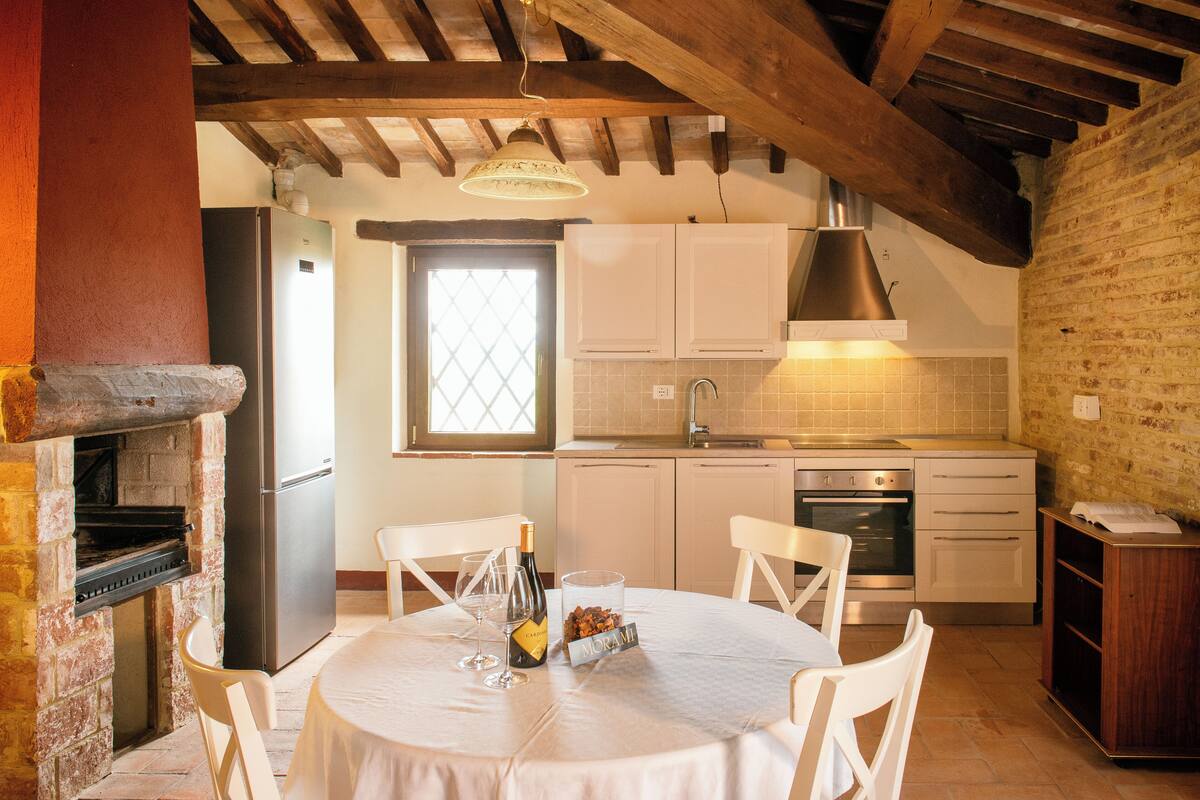 Une cuisine avec des meubles blancs, un four en briques et un coin repas avec une table mise pour deux personnes.