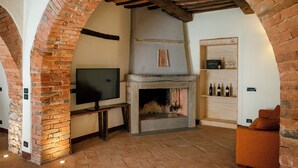 A cozy room with a fireplace, a television, and a wine rack. - Villaluce Wine Agriturismo (Castiglione del Lago)