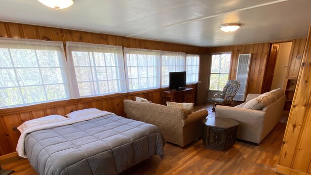Interior de cabana com cama, sofá e televisão.
