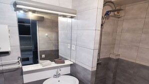 Moderni kylpyhuone, jossa on valkoinen pesuallas, tumma taso ja avoin suihkutila.