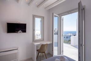 A bedroom with a bed, a TV, a desk, a chair, and a balcony with a view of the sea.