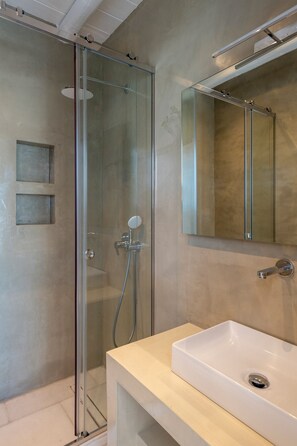 Ein modernes Badezimmer mit einer gläsernen Dusche, einem weißen Waschbecken und einem Spiegel darüber.