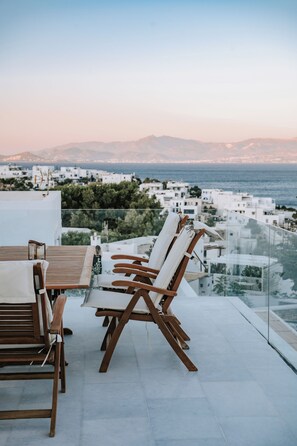 Eine Terrasse mit Tisch und Stühlen, mit Blick auf eine Küstenstadt mit weißen Häusern und Meerblick.
