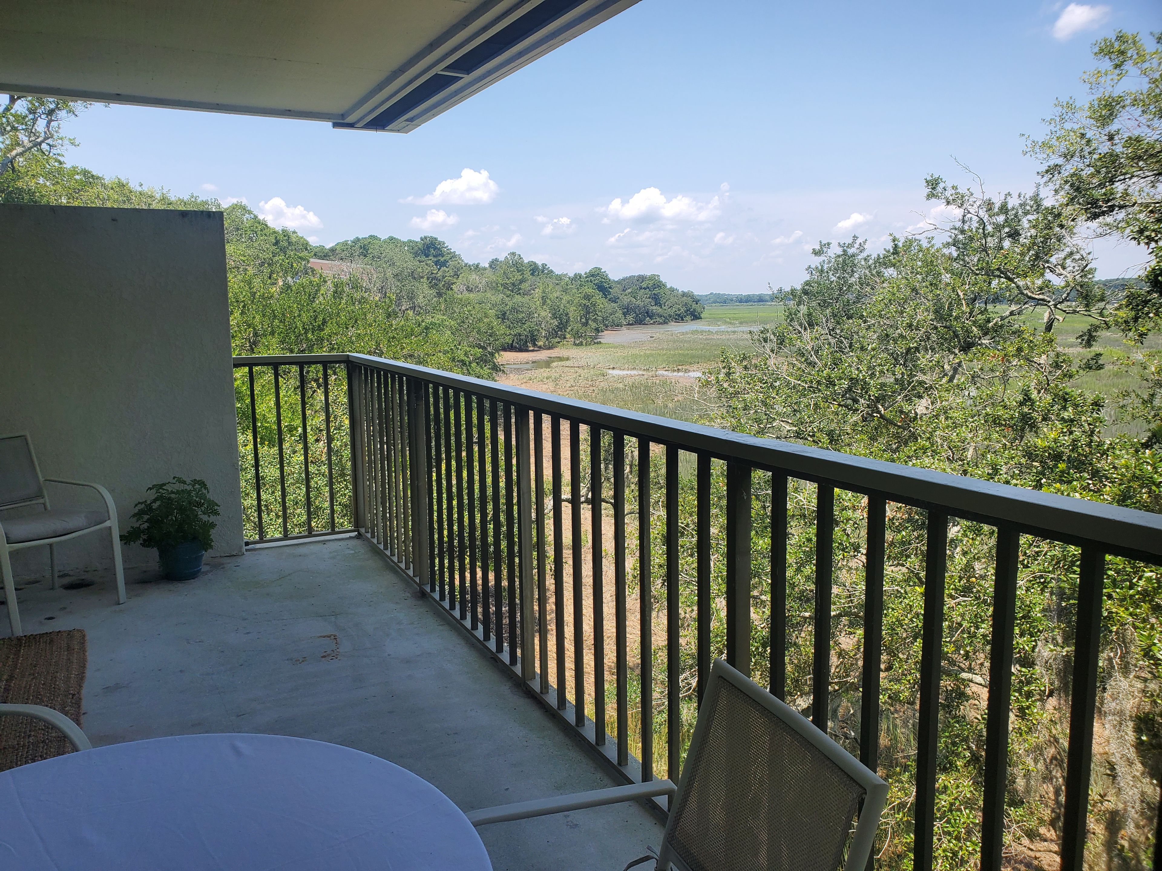 A balcony with a table and chairs, overlooking a green landscape with trees and a field.
