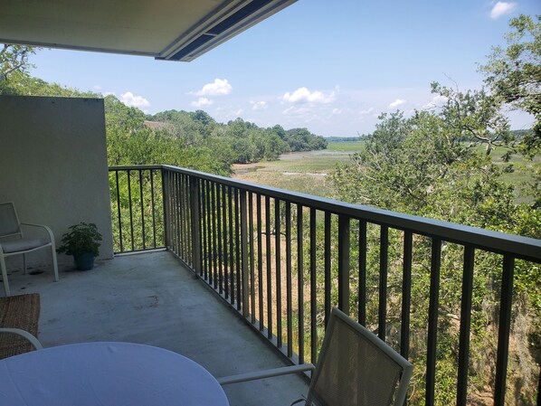 A balcony with a table and chairs, overlooking a green landscape with trees and a field.