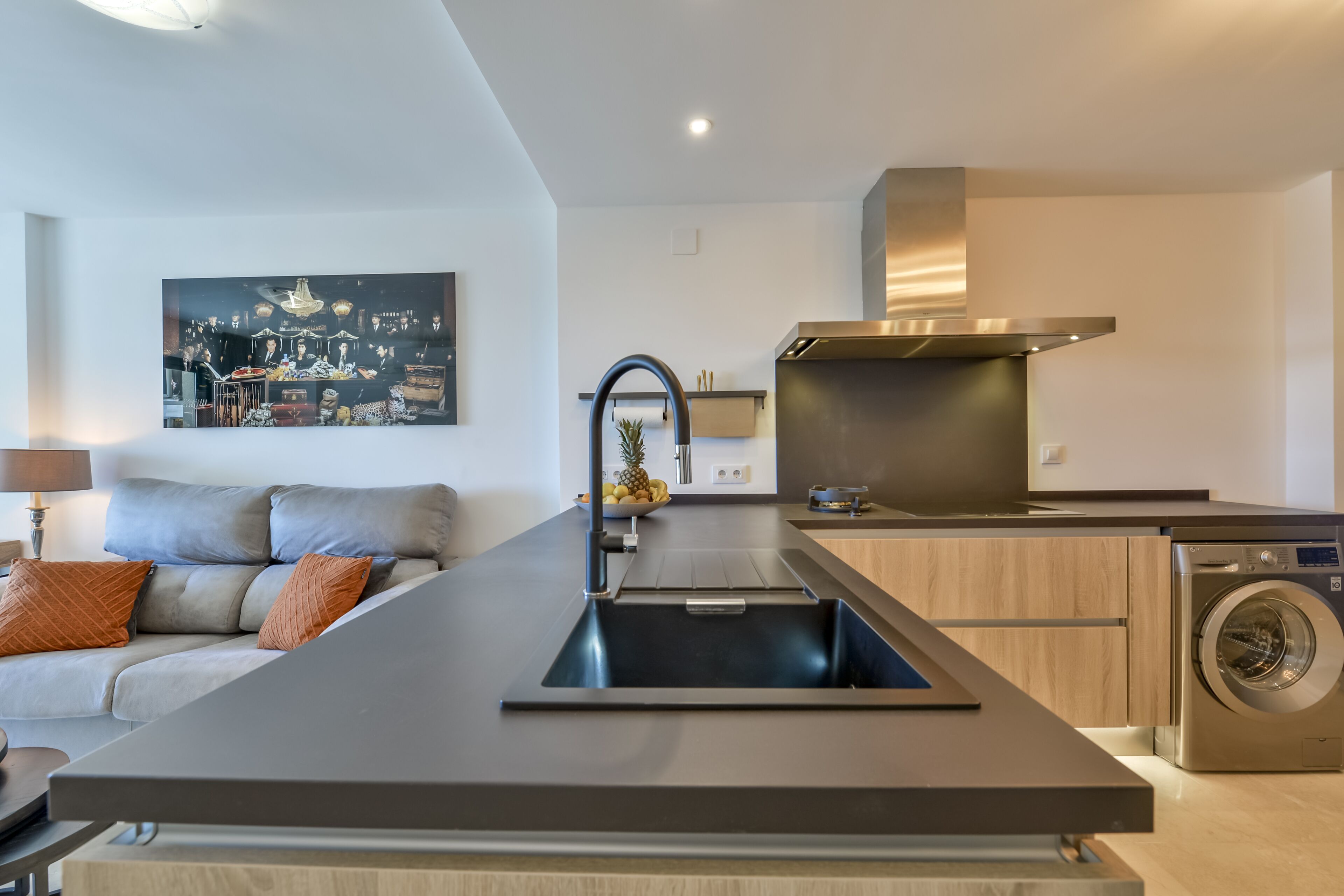 A modern kitchen with a central island, built-in appliances, and a dining area with a sofa and a painting.